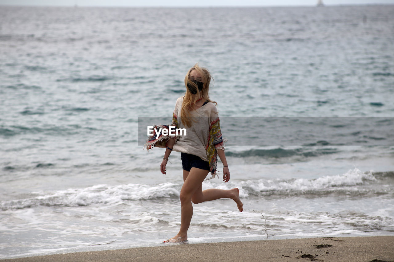 FULL LENGTH REAR VIEW OF WOMAN STANDING AT BEACH