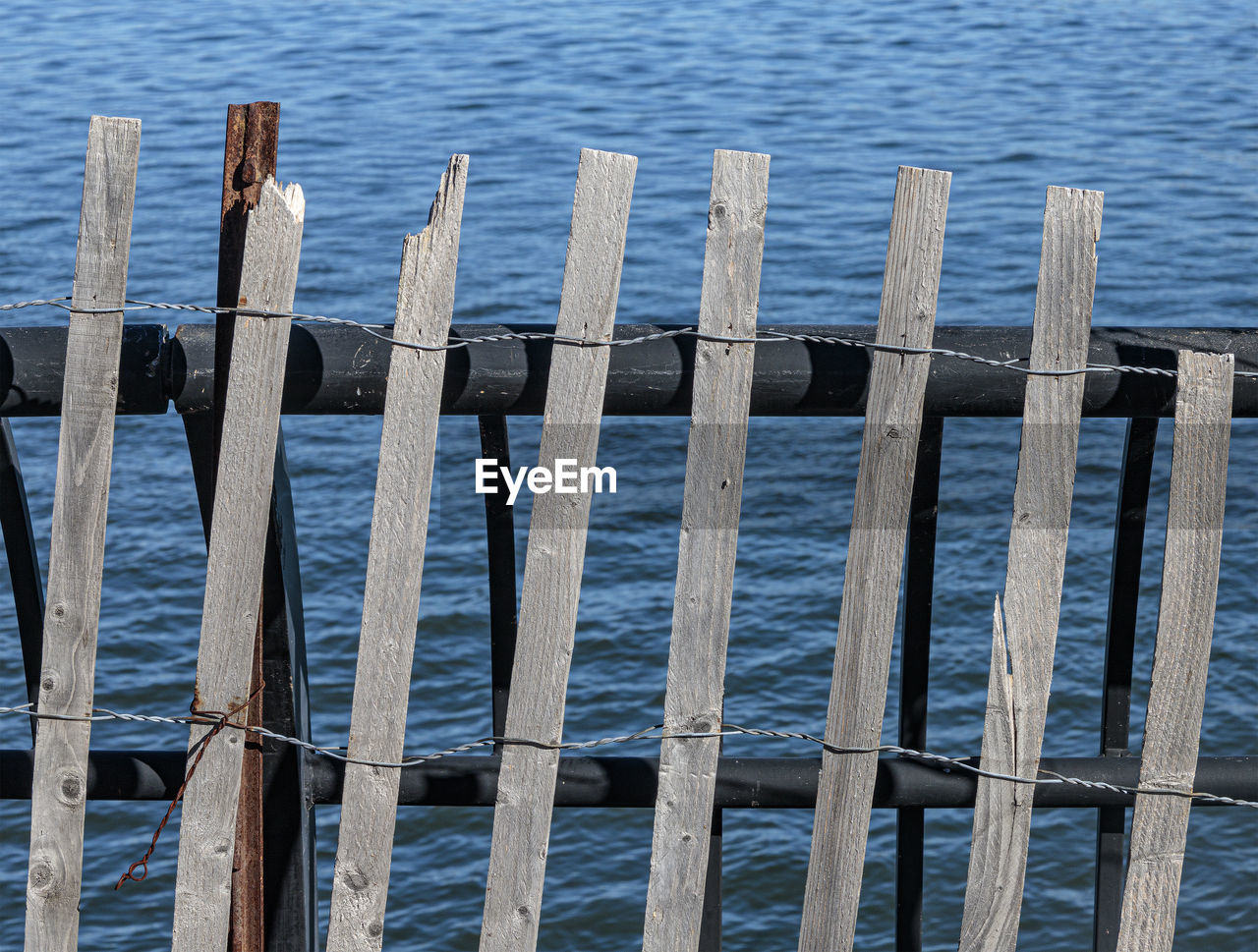 water, wood, fence, blue, sea, no people, nature, day, home fencing, security, tranquility, outdoors, beach, land, protection, iron, reflection, beauty in nature, tranquil scene, high angle view, pier, in a row, scenics - nature, outdoor structure, wooden post