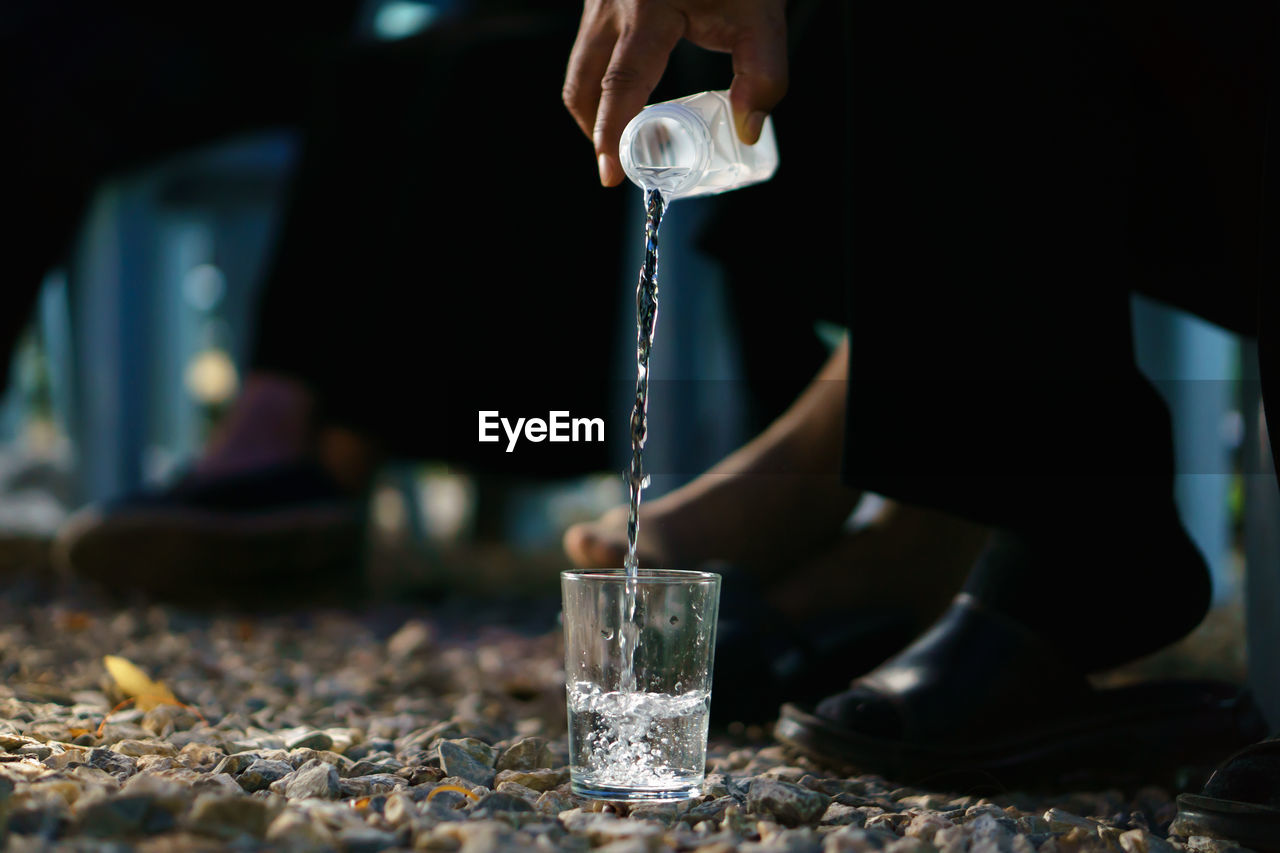 Cropped hand of man pouring drink in drinking glass on stones