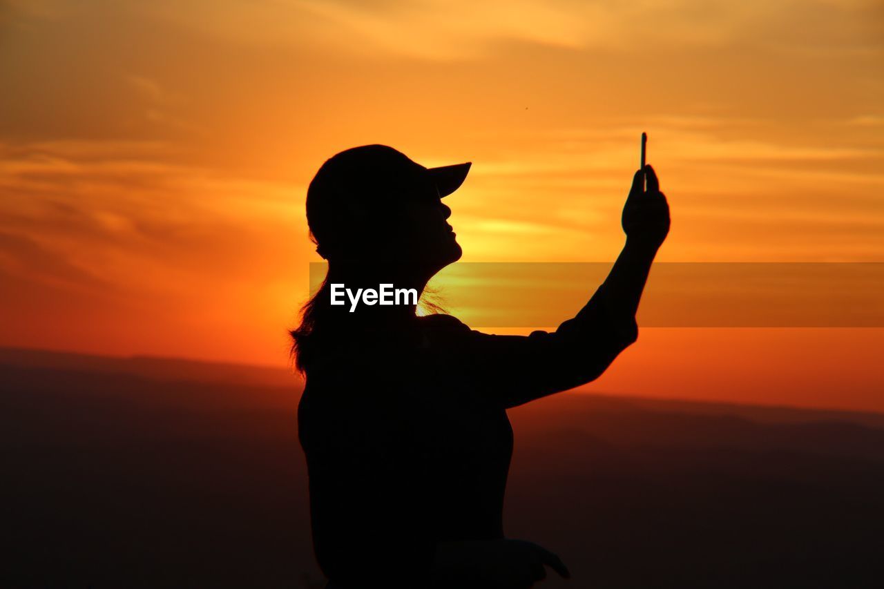 Silhouette woman taking selfie against orange sky during sunset