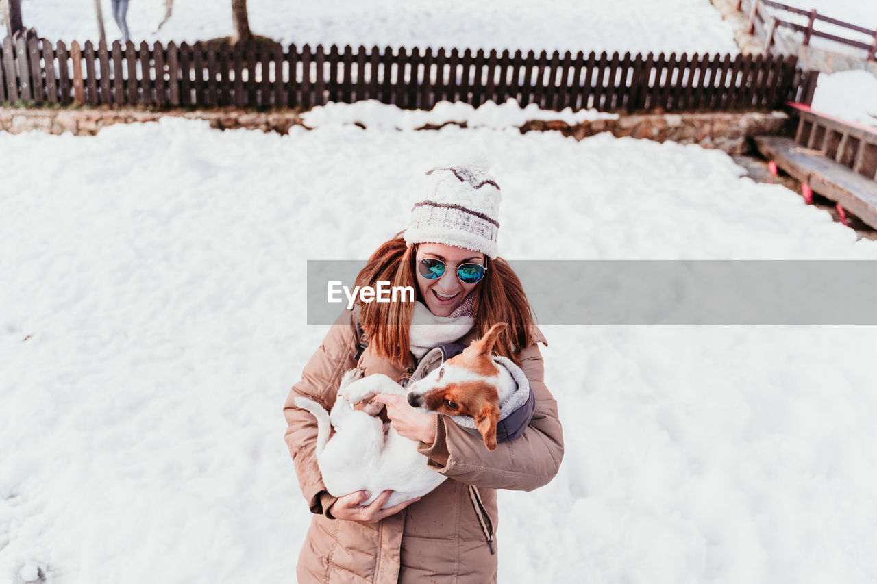 Cheerful woman carrying dog while standing on snowy land