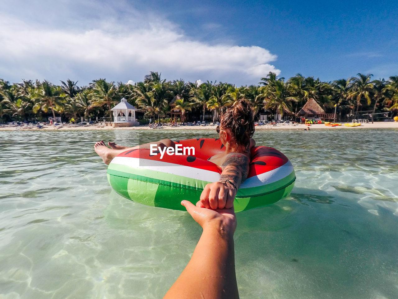 Cropped hand of woman holding female friend floating on inflatable ring in sea