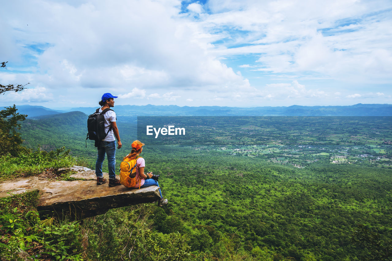 Rear view of man and woman standing on cliff against sky