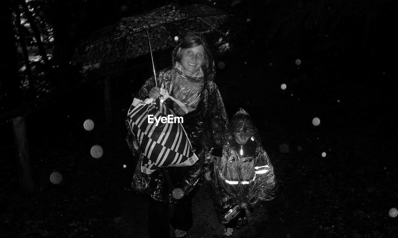 Young woman with umbrella and son walking through the rain at night