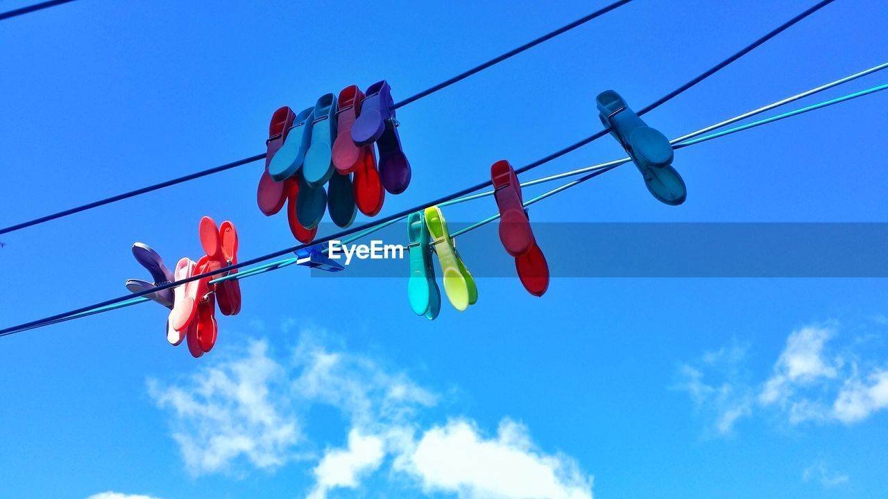 Low angle view of clothespins hanging on rope against blue sky