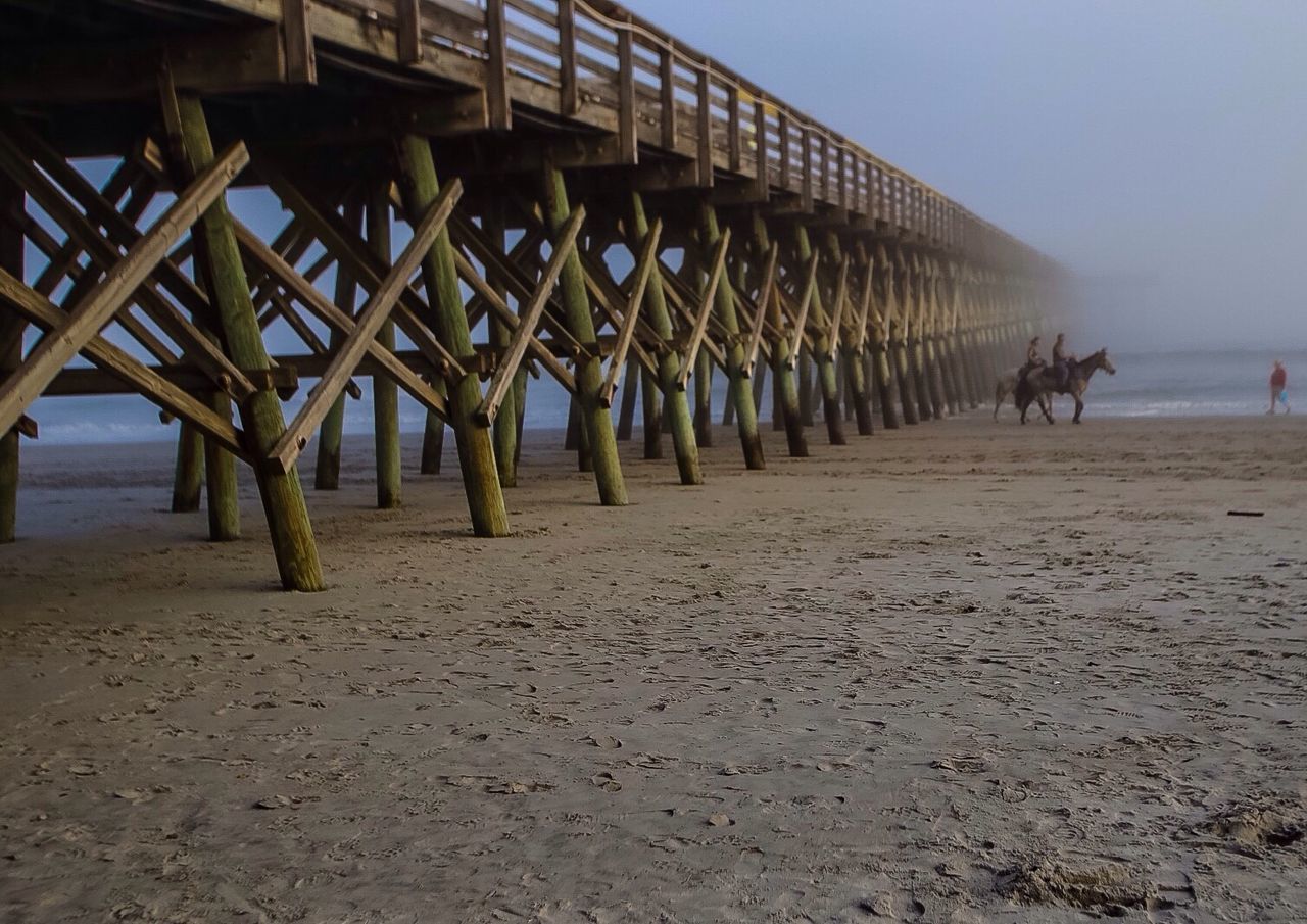 People riding horse by pier at beach during foggy weather
