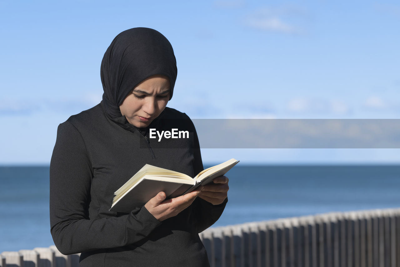 Focused muslim woman reading a book outdoors