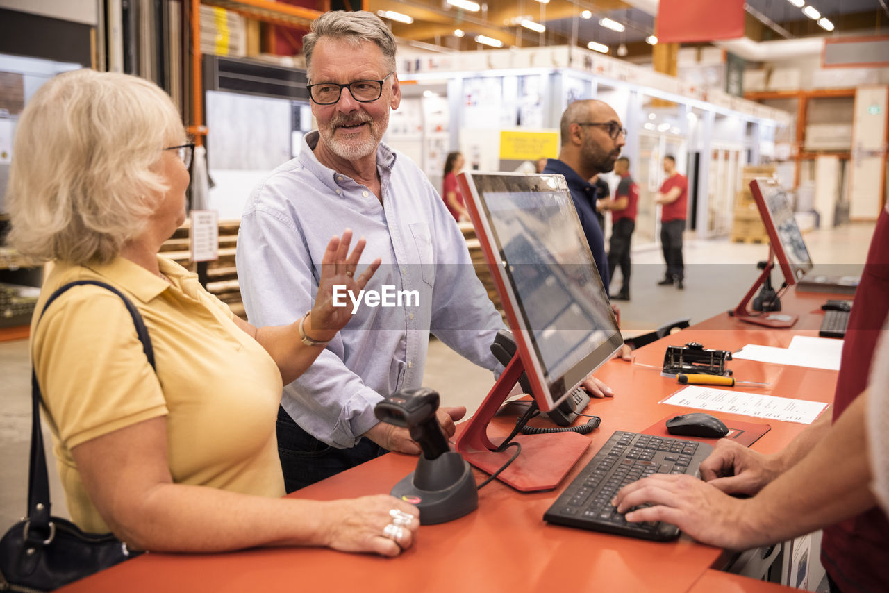 Senior male and female customers talking with each other while standing at checkout counter in hardware store