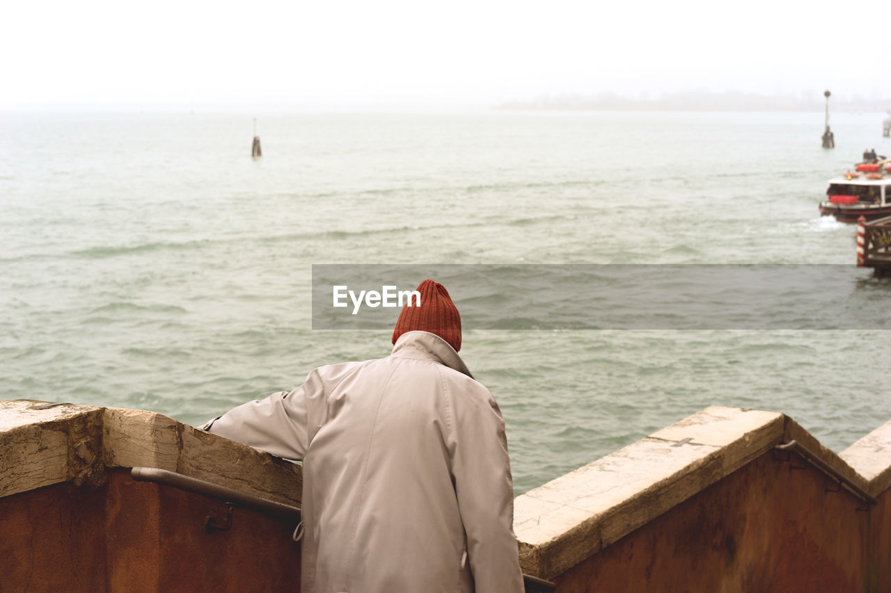 Rear view of man by retaining wall against sea