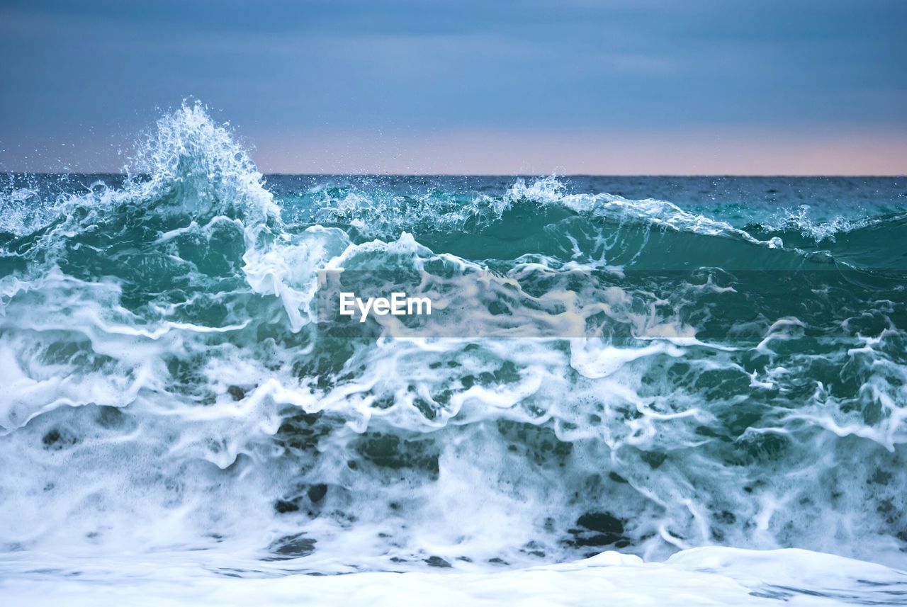 VIEW OF SEA WAVES SPLASHING ON SHORE AGAINST SKY