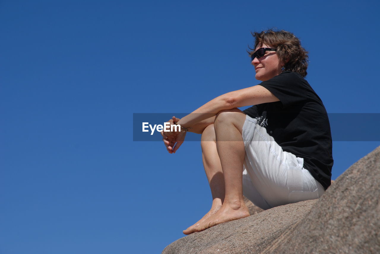 Low angle view of woman sitting on rock at magnetic island against clear sky