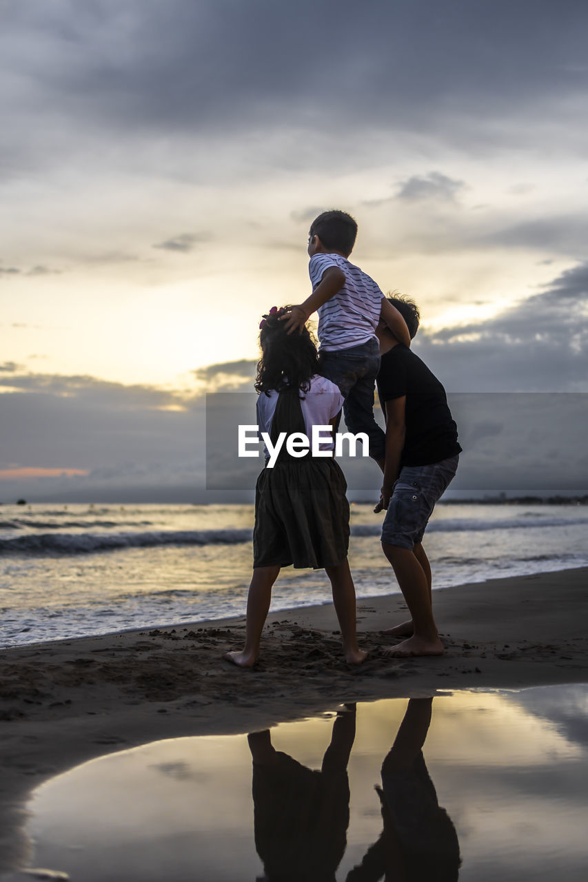 Rear view of couple on beach against sky during sunset