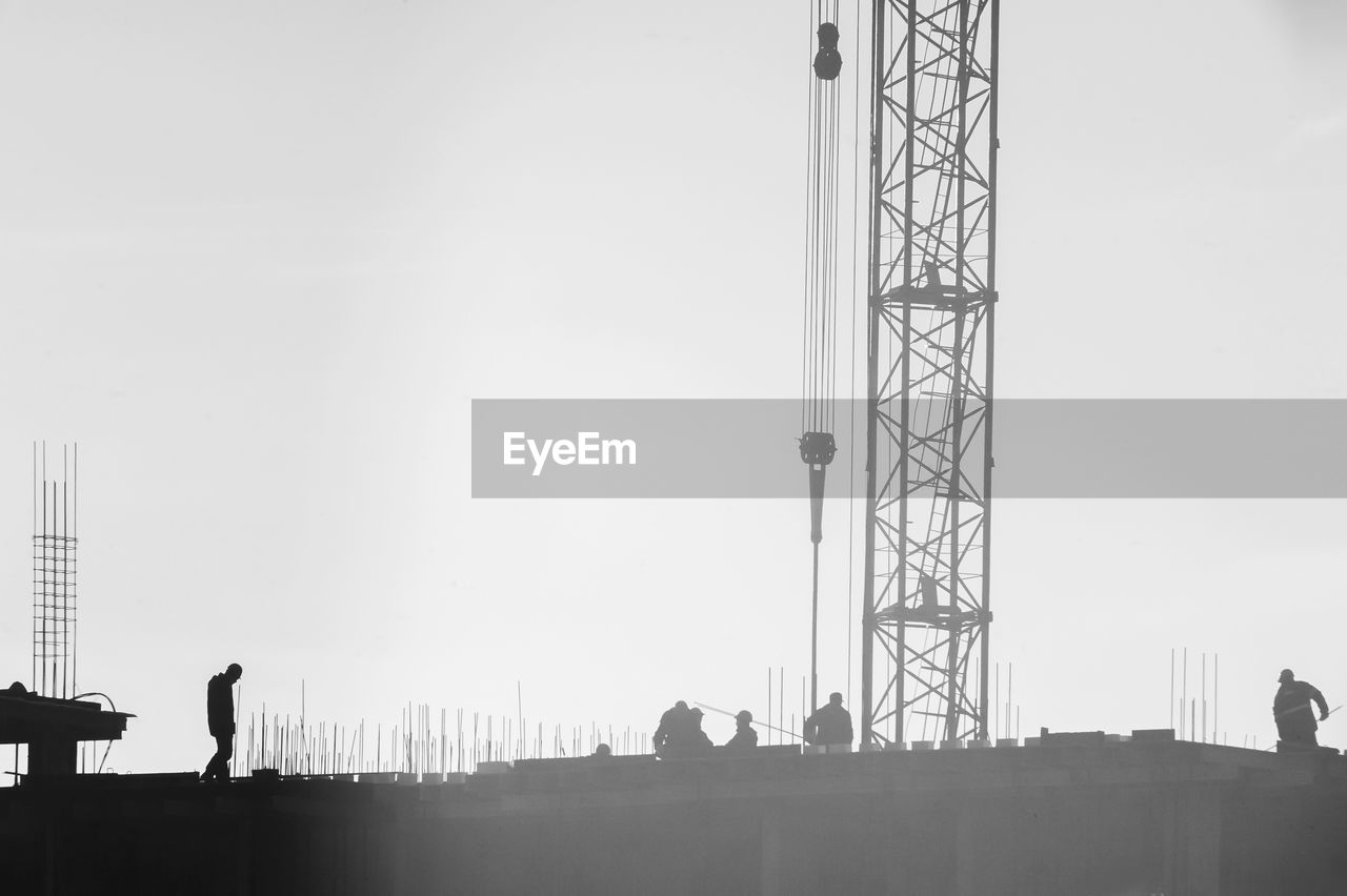Silhouette people at construction site against clear sky