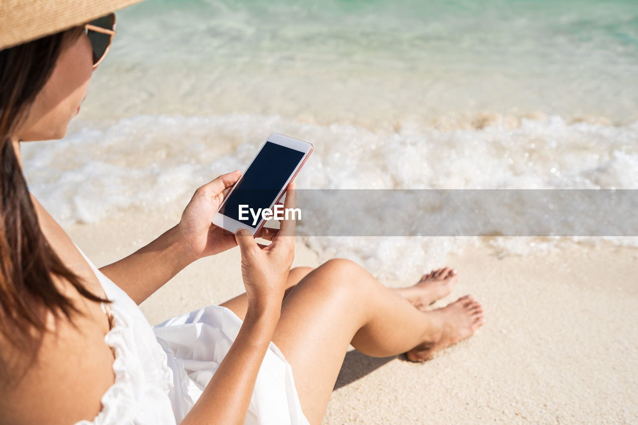 MIDSECTION OF WOMAN USING PHONE ON BEACH