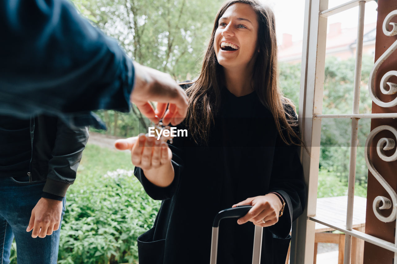 Smiling woman receiving house keys from owner while standing at doorway