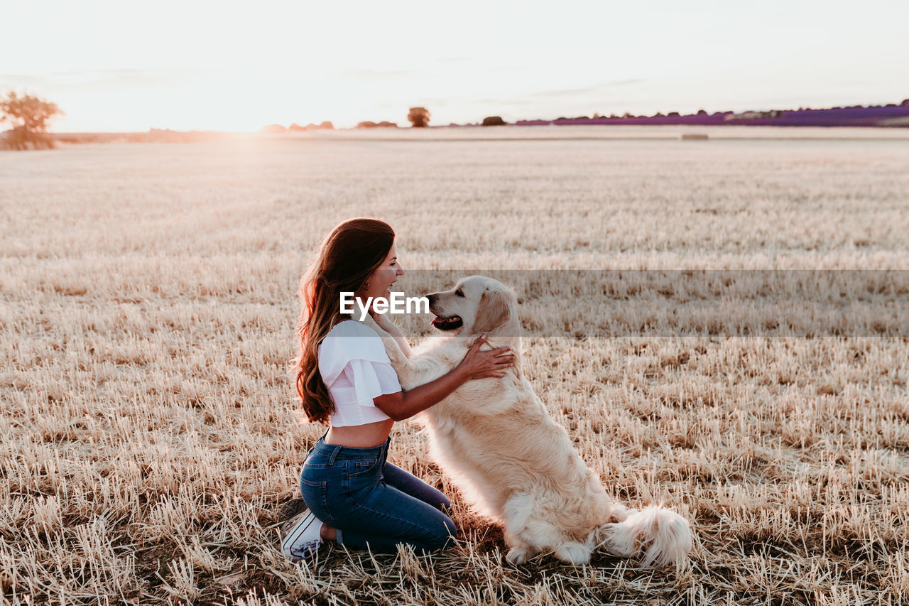 Side view of woman with dog on landscape during sunset