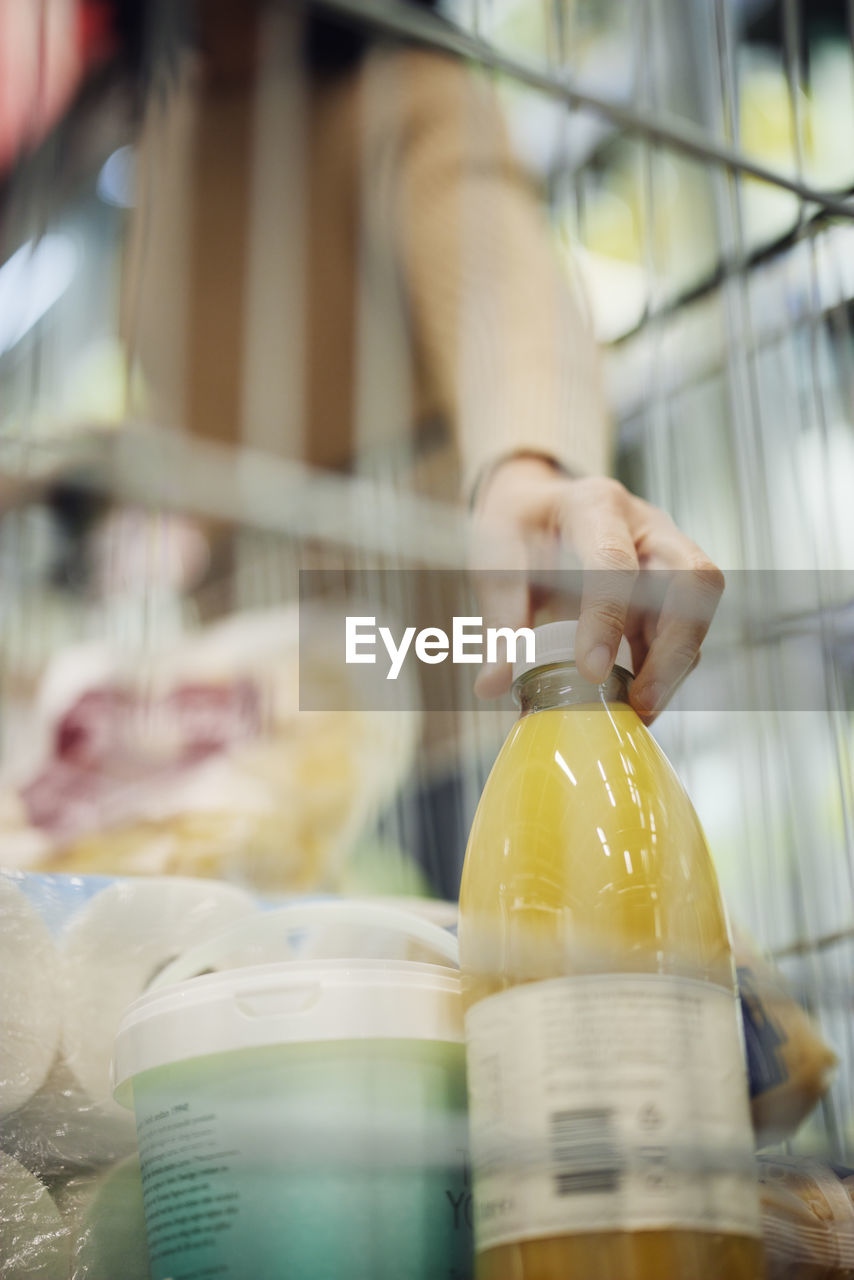 Woman's hand putting juice bottle into shopping trolley