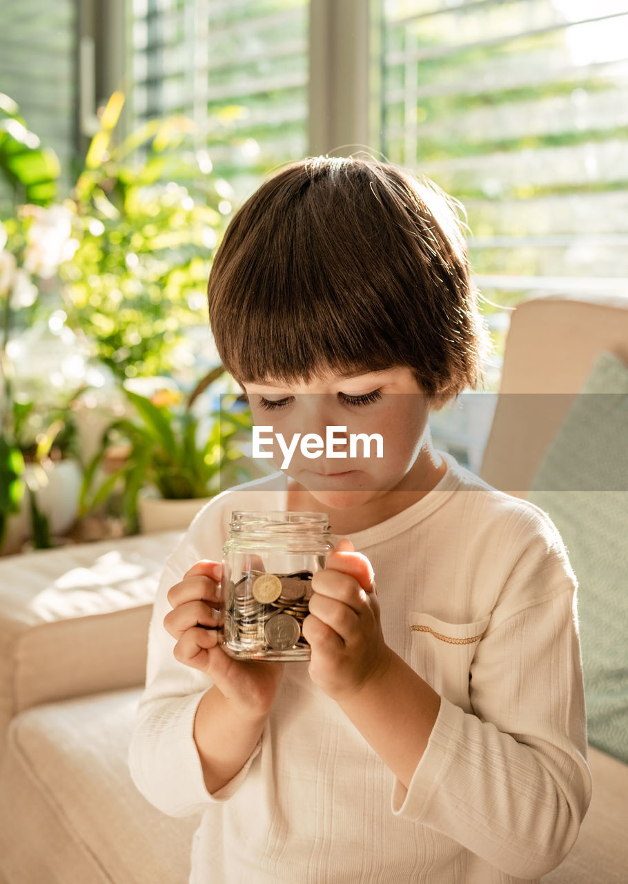 Happy little child holding glass jar full of coins. kid counting money saving from change learning