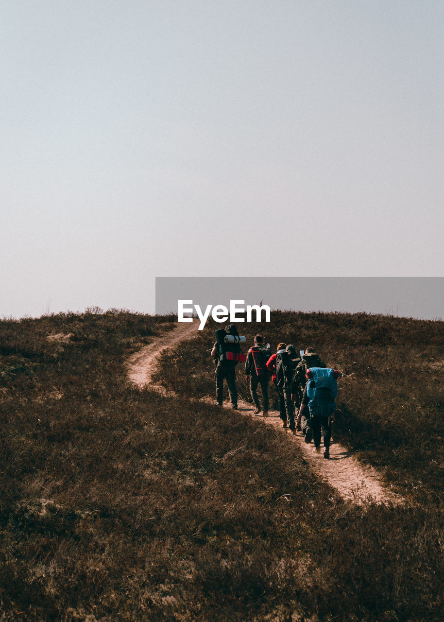 Rear view of people walking on mountain against clear sky