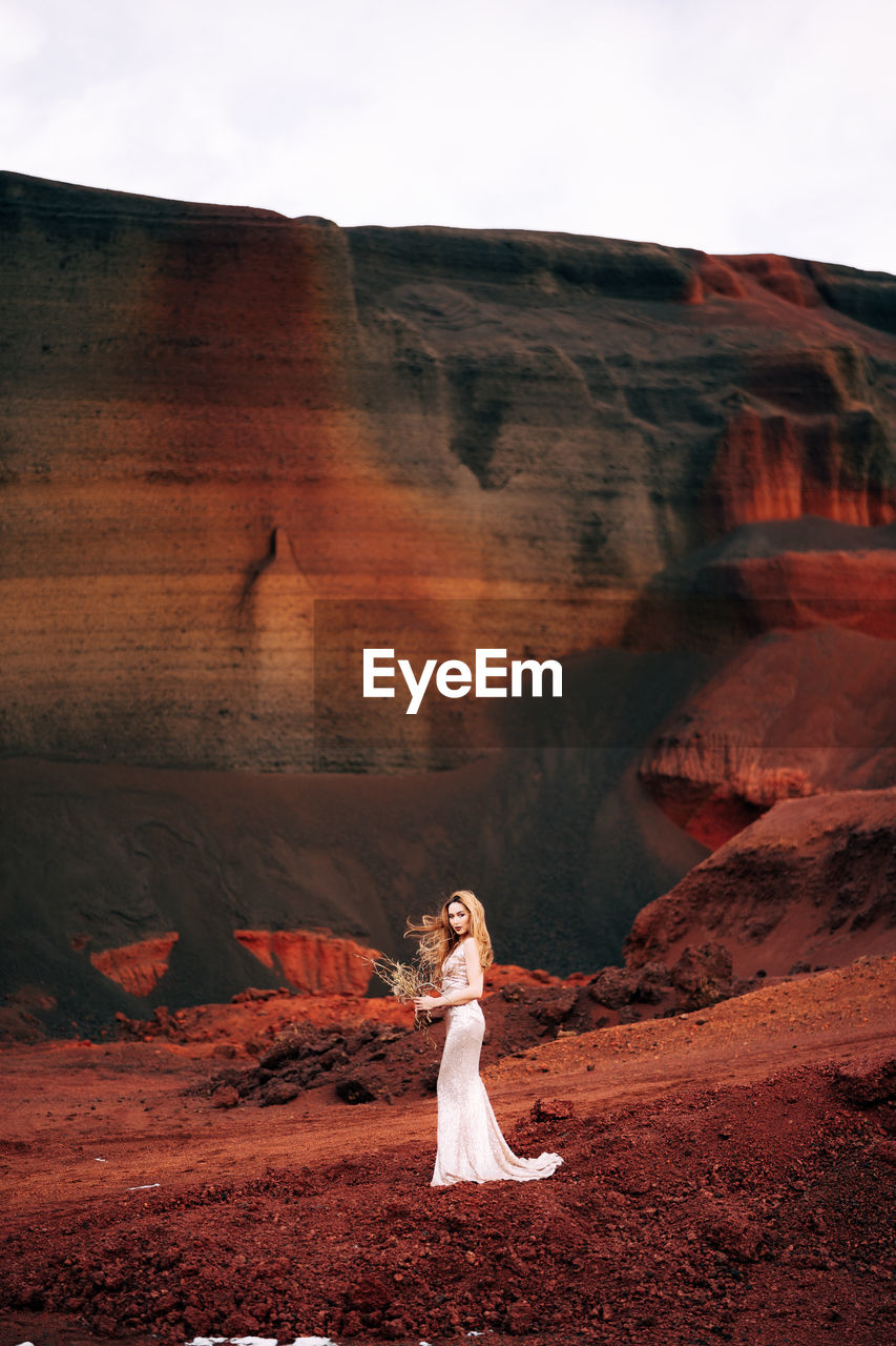 WOMAN STANDING ON ROCK FORMATION IN SUNLIGHT