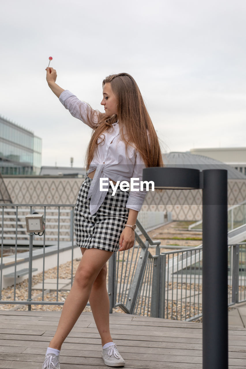 Woman with lollipop standing on boardwalk against sky