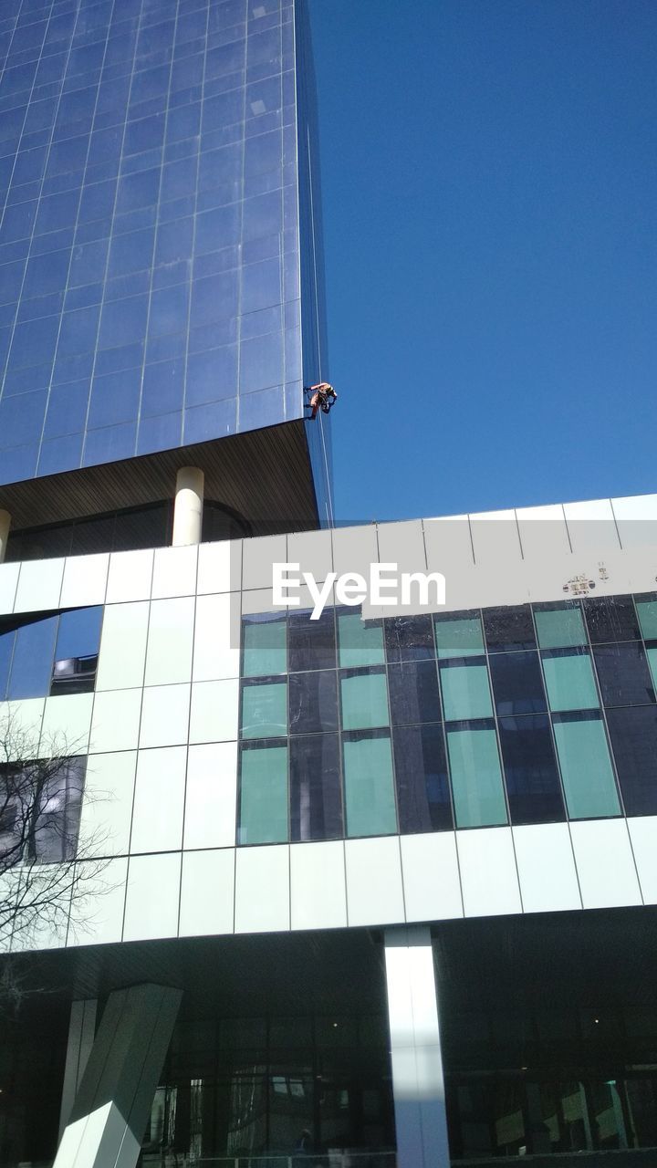 LOW ANGLE VIEW OF MODERN GLASS BUILDING AGAINST CLEAR BLUE SKY