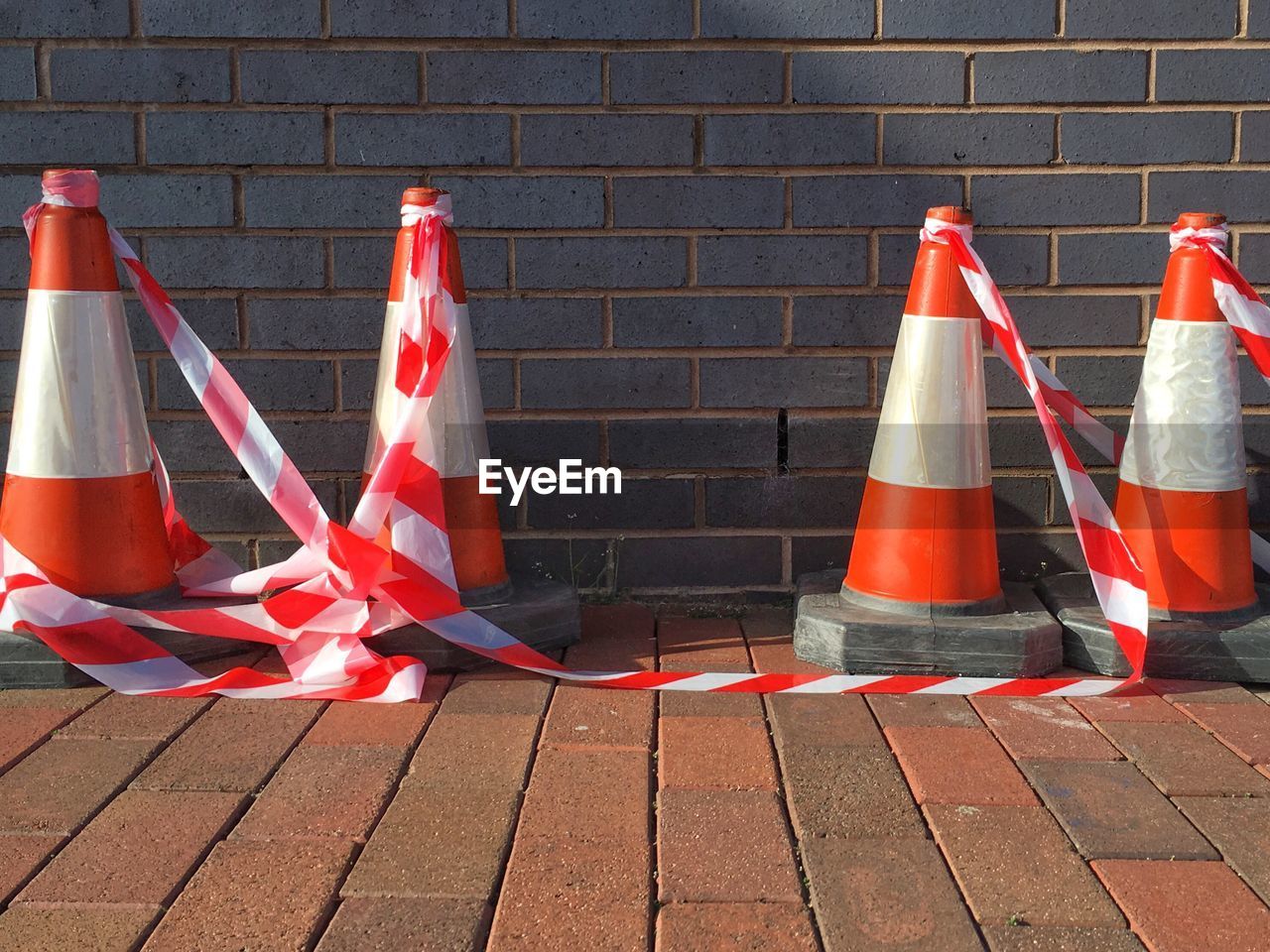 Traffic cones with cordon tape on footpath against wall