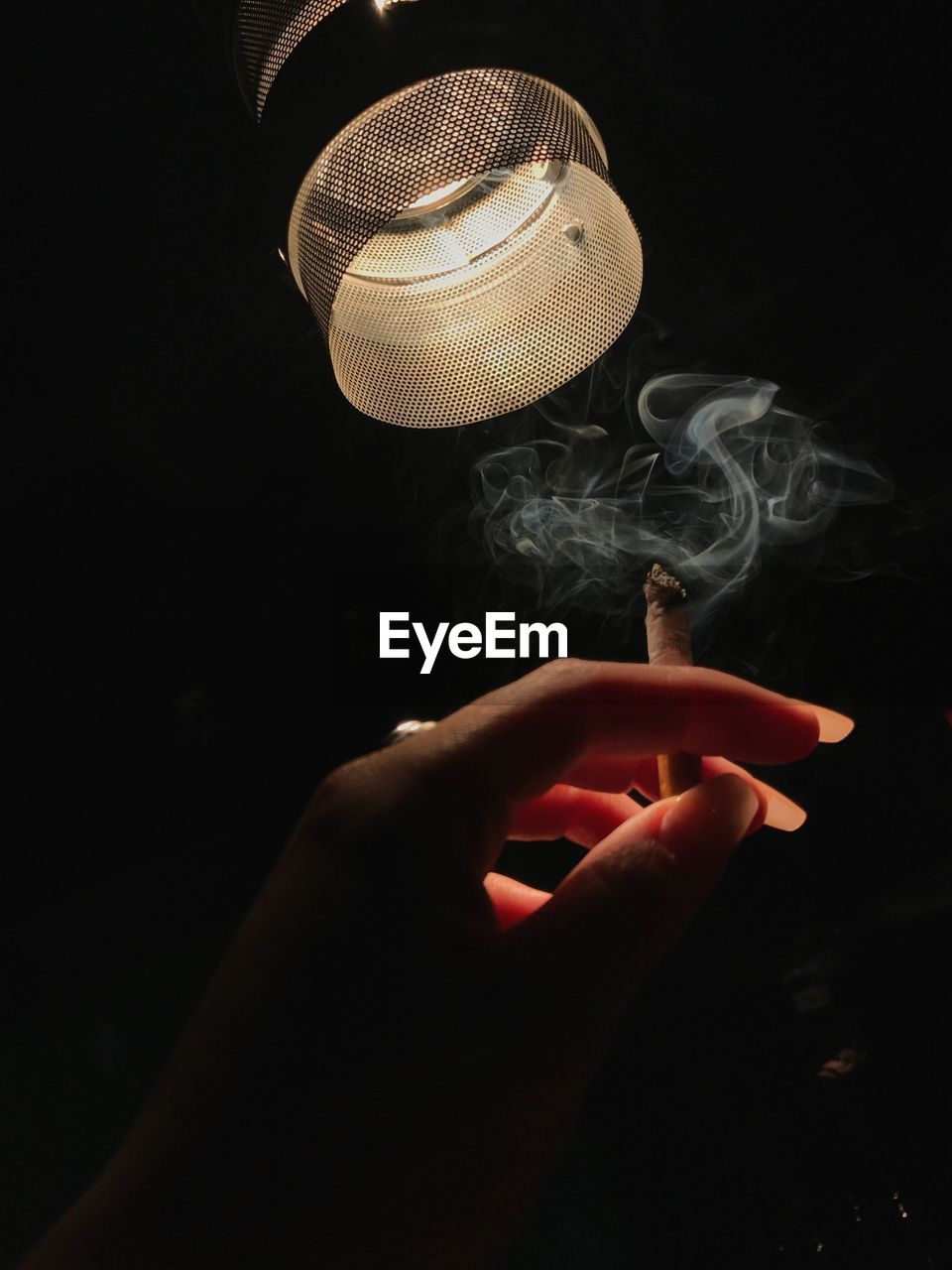 Cropped hand of woman holding cigarette against black background