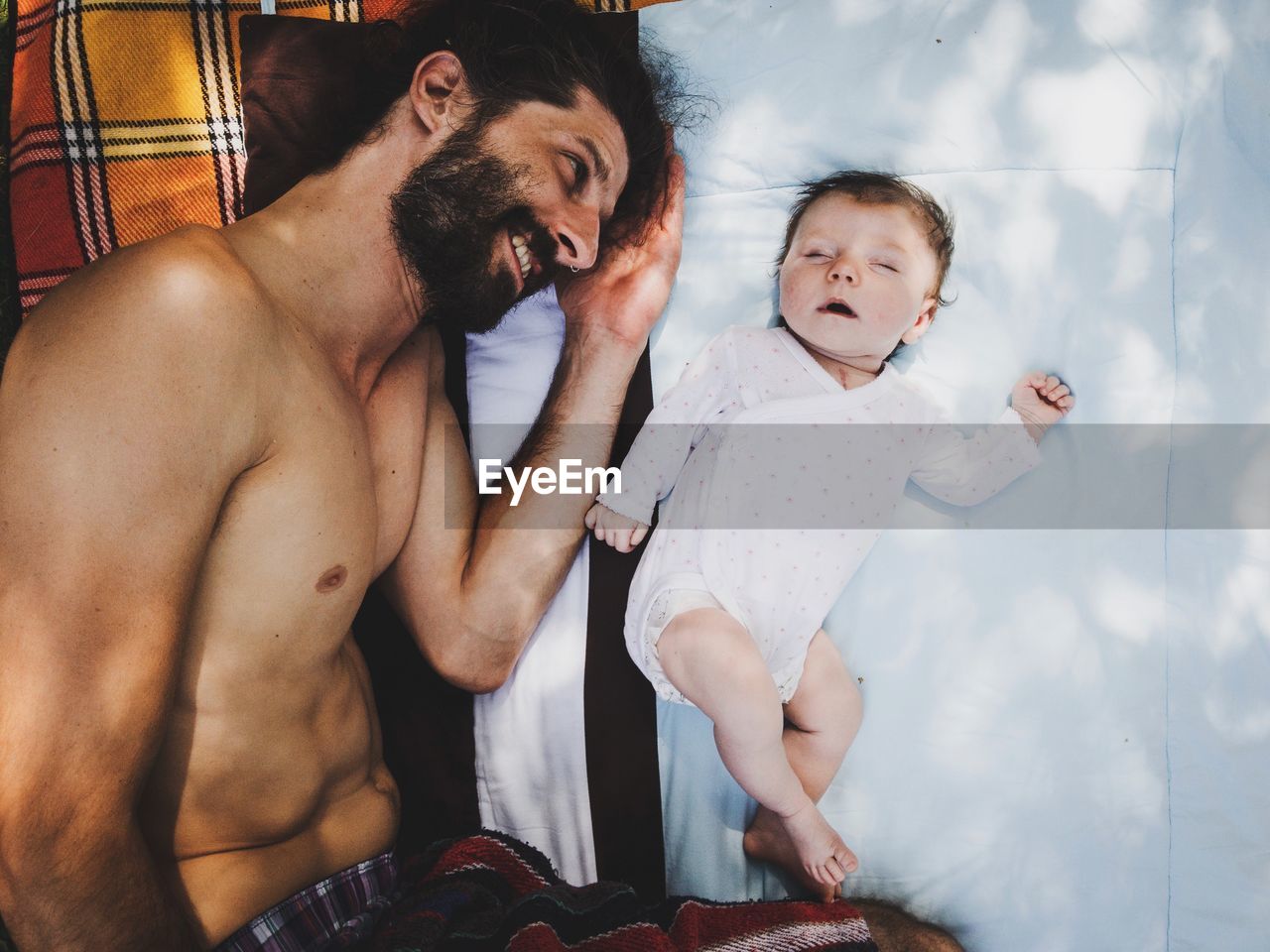 Directly above shot of shirtless father lying with toddler daughter on bed