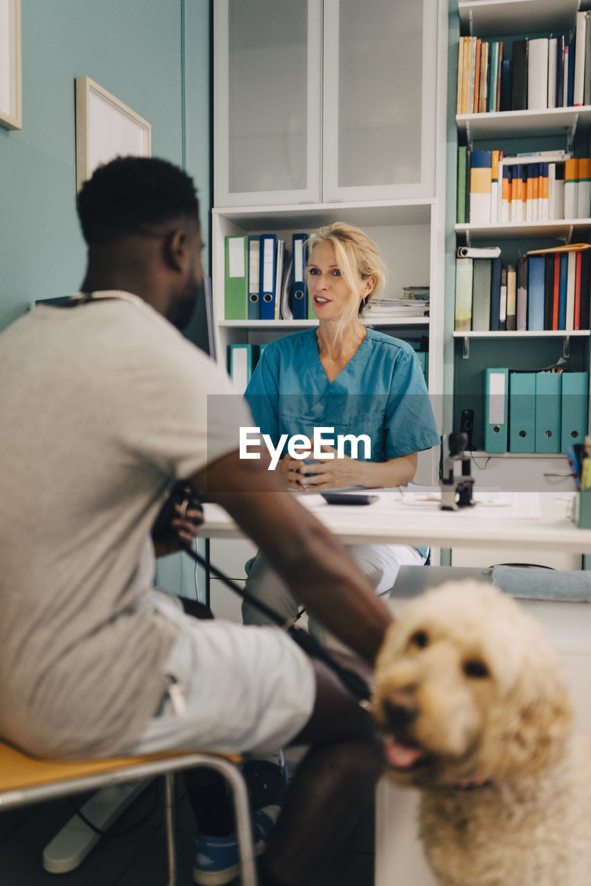 Young man with dog talking to female veterinarian at desk in medical clinic