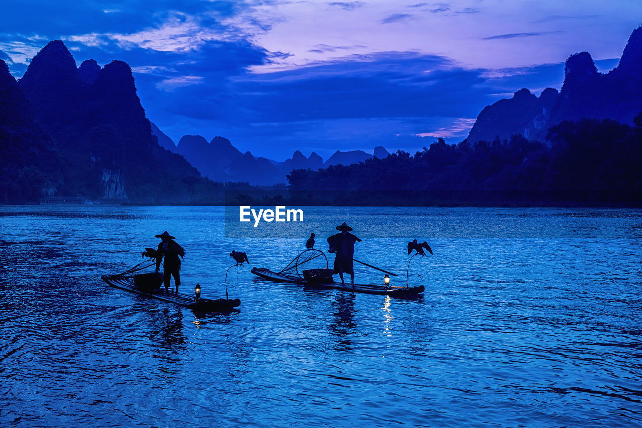 Men with birds on wooden raft in lake