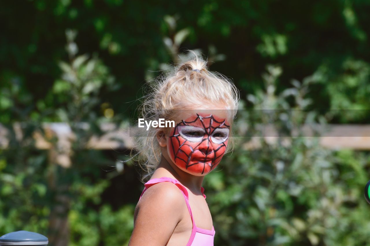 Portrait of girl with painted face standing against plants