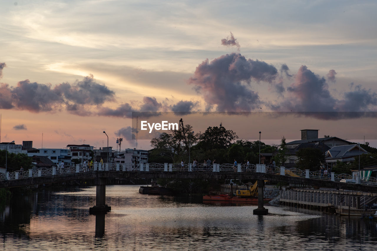 Bridge over river by buildings against sky during sunset