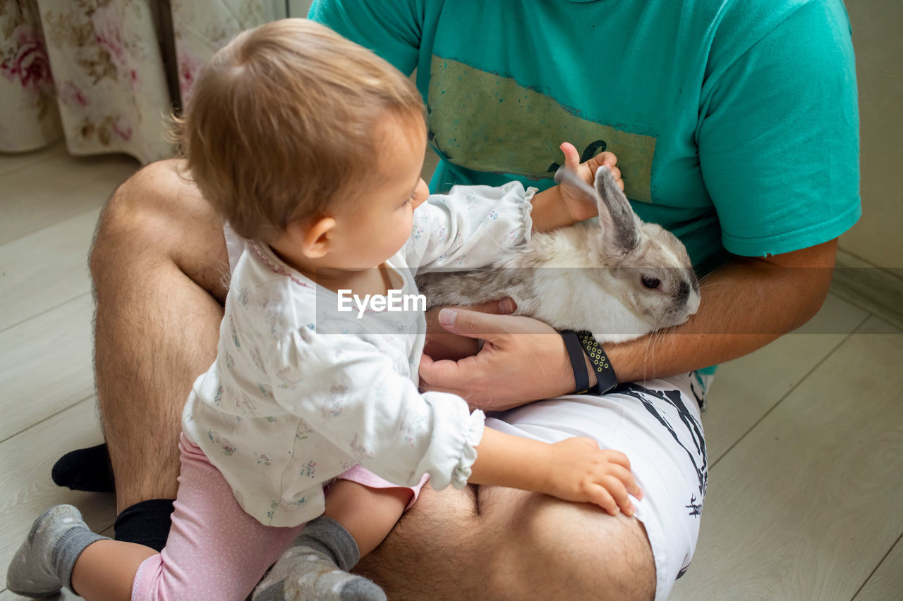 Midsection of father with baby and rabbit at home