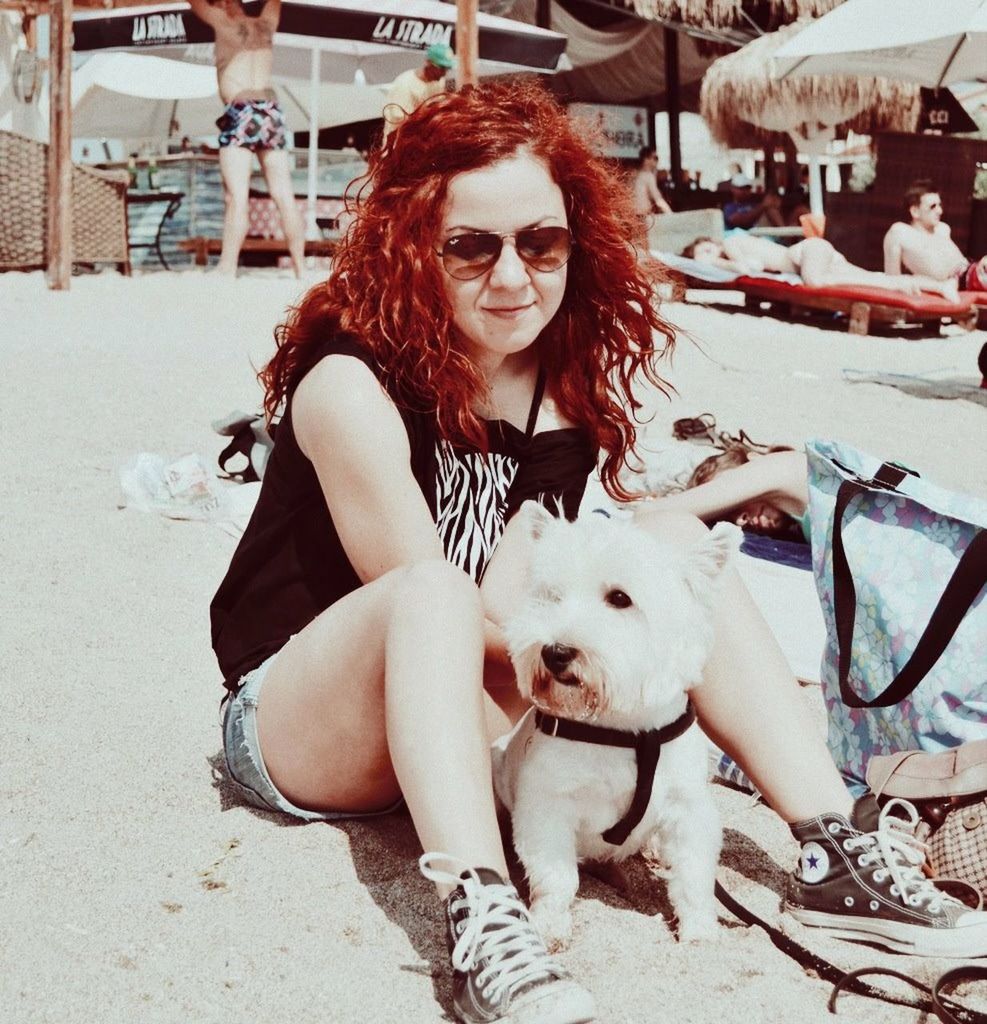 Red hair woman sitting with dog on sand by beach