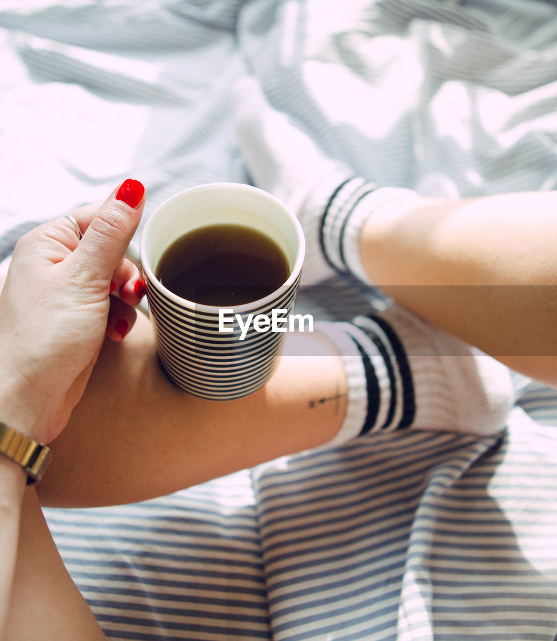 Personal perspective of woman holding coffee cup on bed