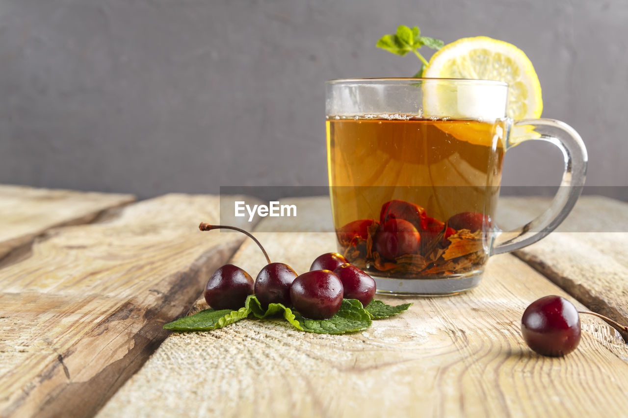 Black tea in a glass cup with mint cherries and lemon on a wooden table near fresh cherries