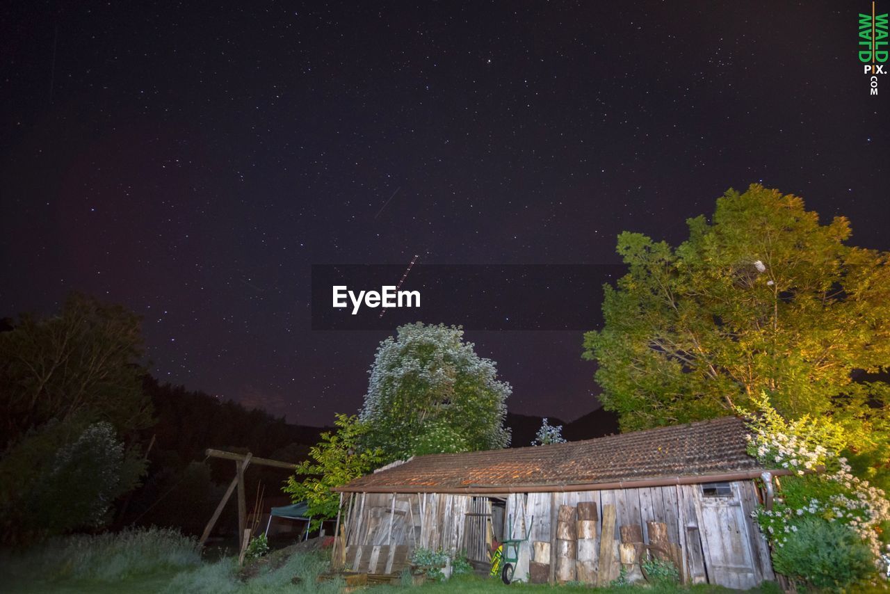 HOUSE BY TREES AGAINST SKY AT NIGHT