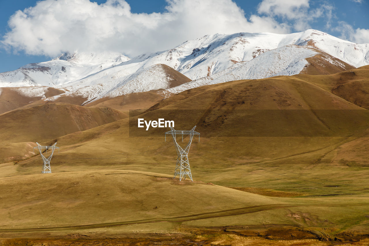 Pylons of high-voltage power lines in the mountains, snowy mountain peaks and blue sky