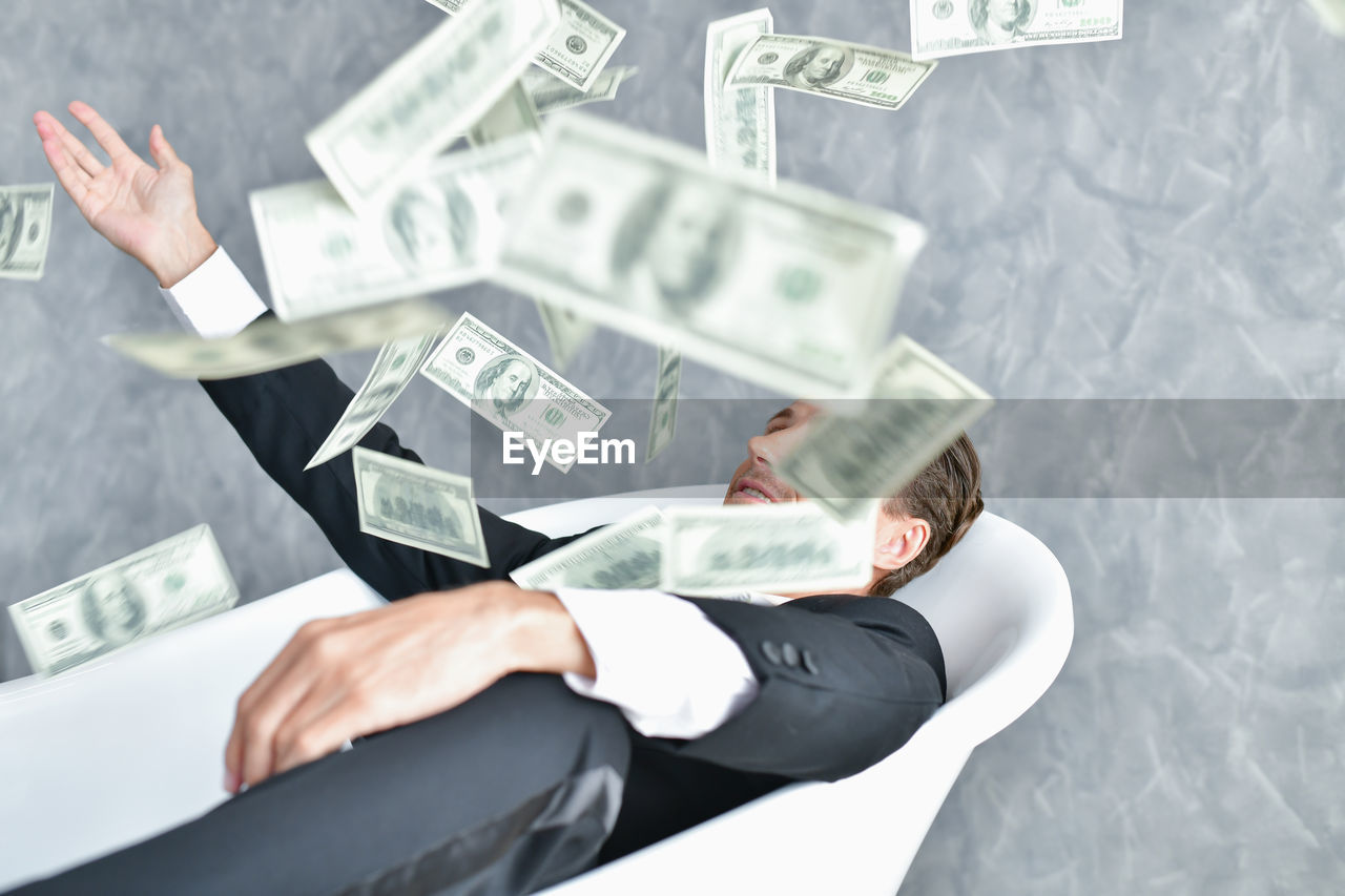 Businessman looking at paper currencies in mid-air while sitting on chair