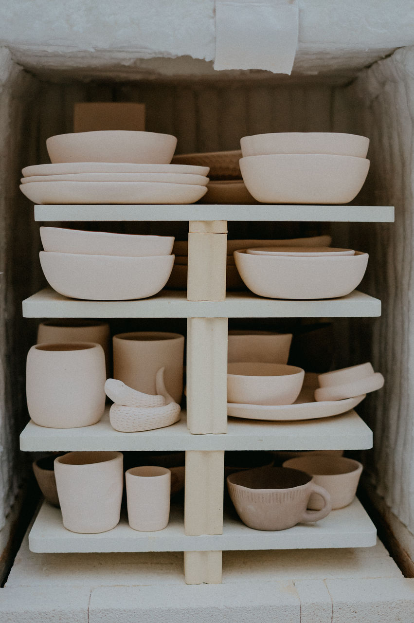 Collection of various ceramic pots and earthenware placed on wooden shelves in art studio