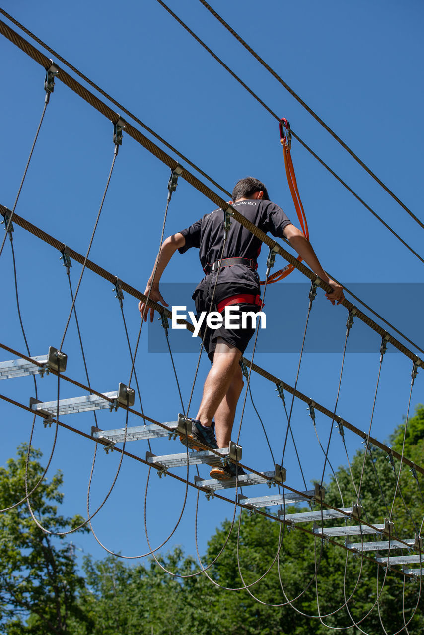 Low angle view of man climbing on cable against sky