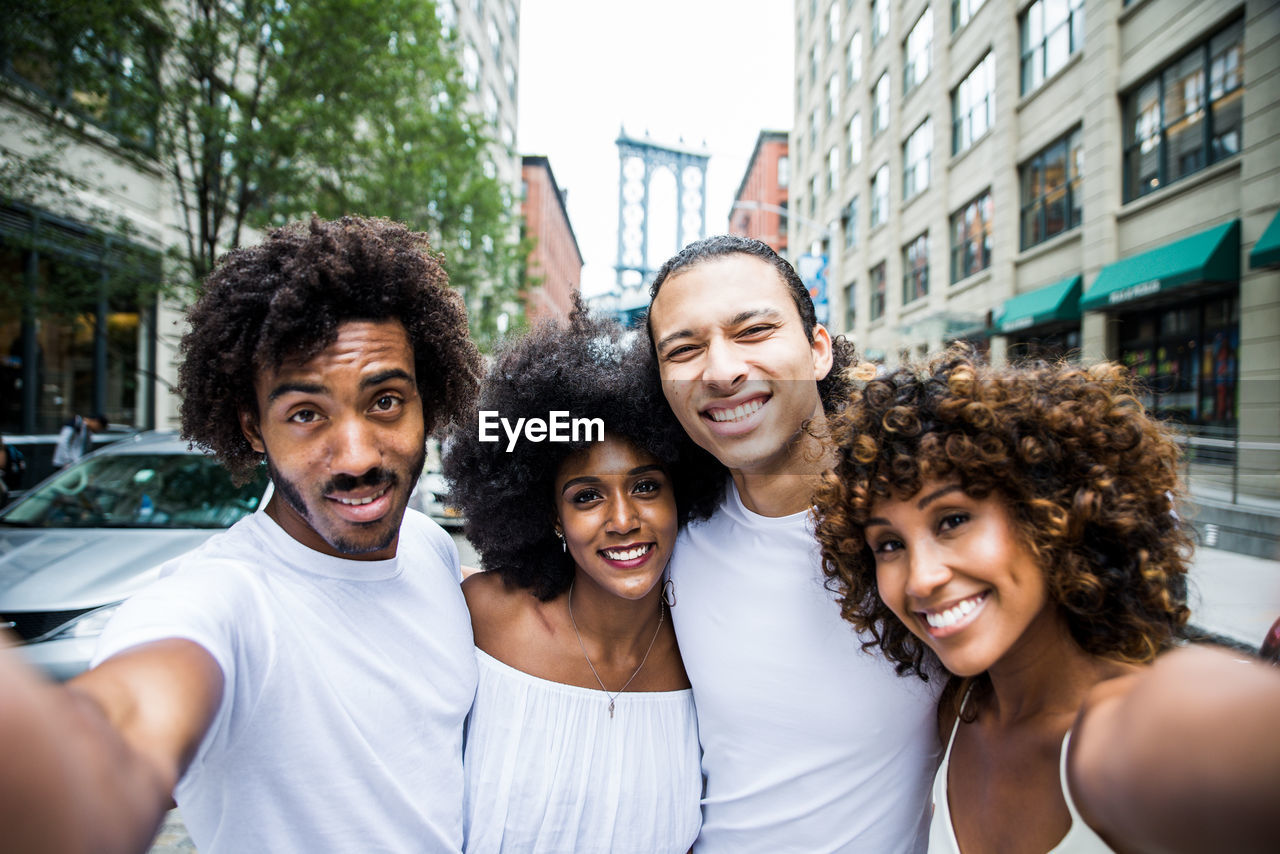 Portrait of smiling friends standing on street in city