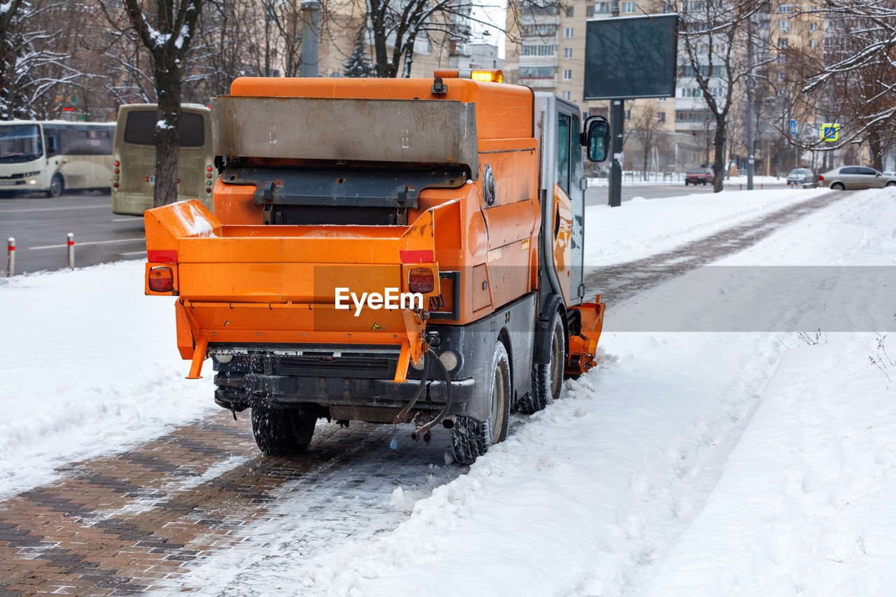 The sweeper cleans the snow on the cobbled sidewalk of the city street.