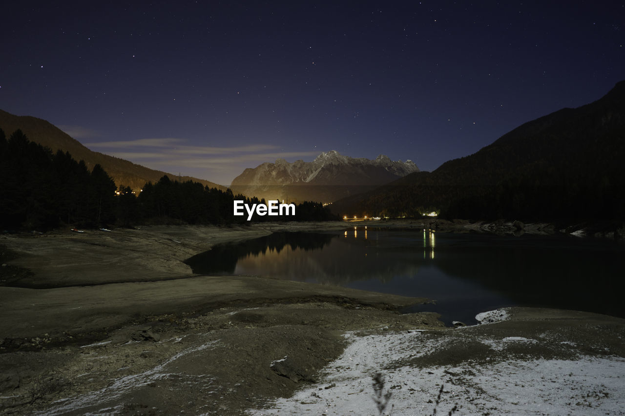 Scenic view of lake by mountains against sky at night