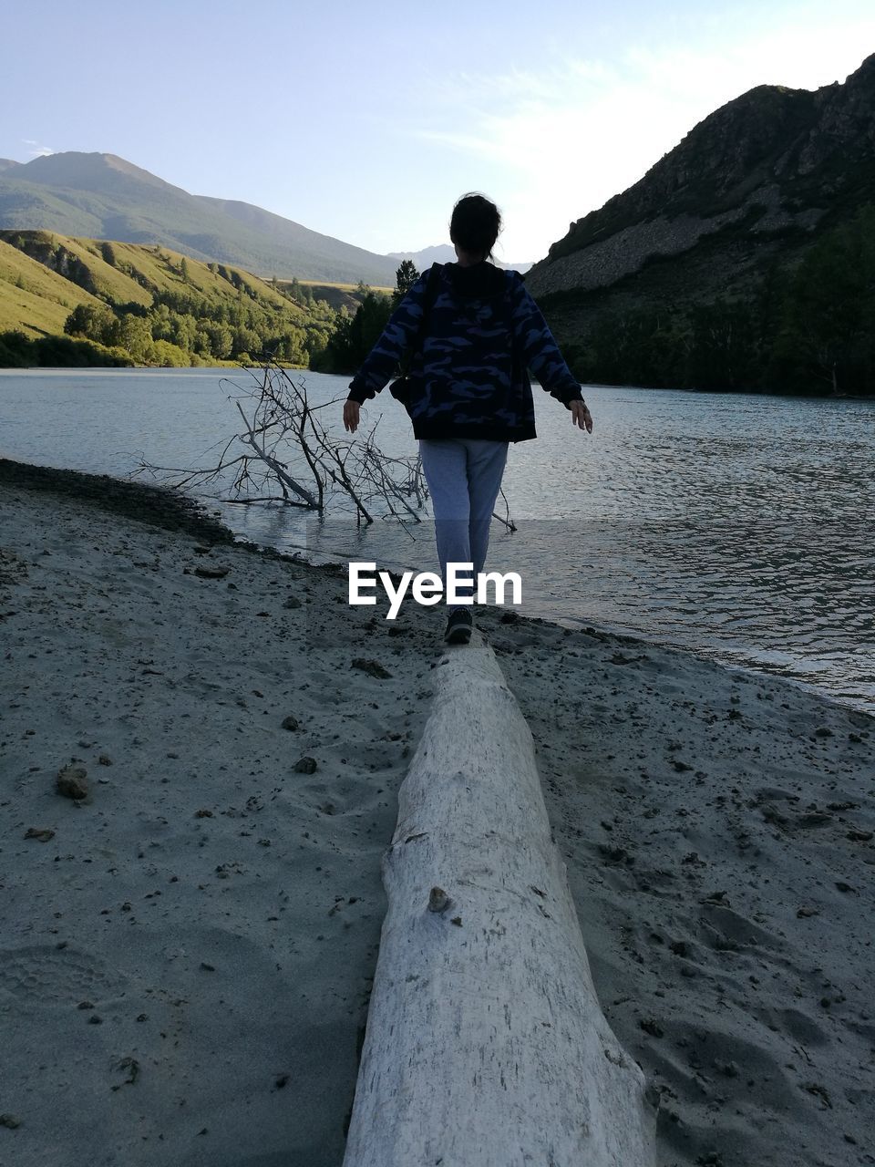 Young woman walking on driftwood at riverbank