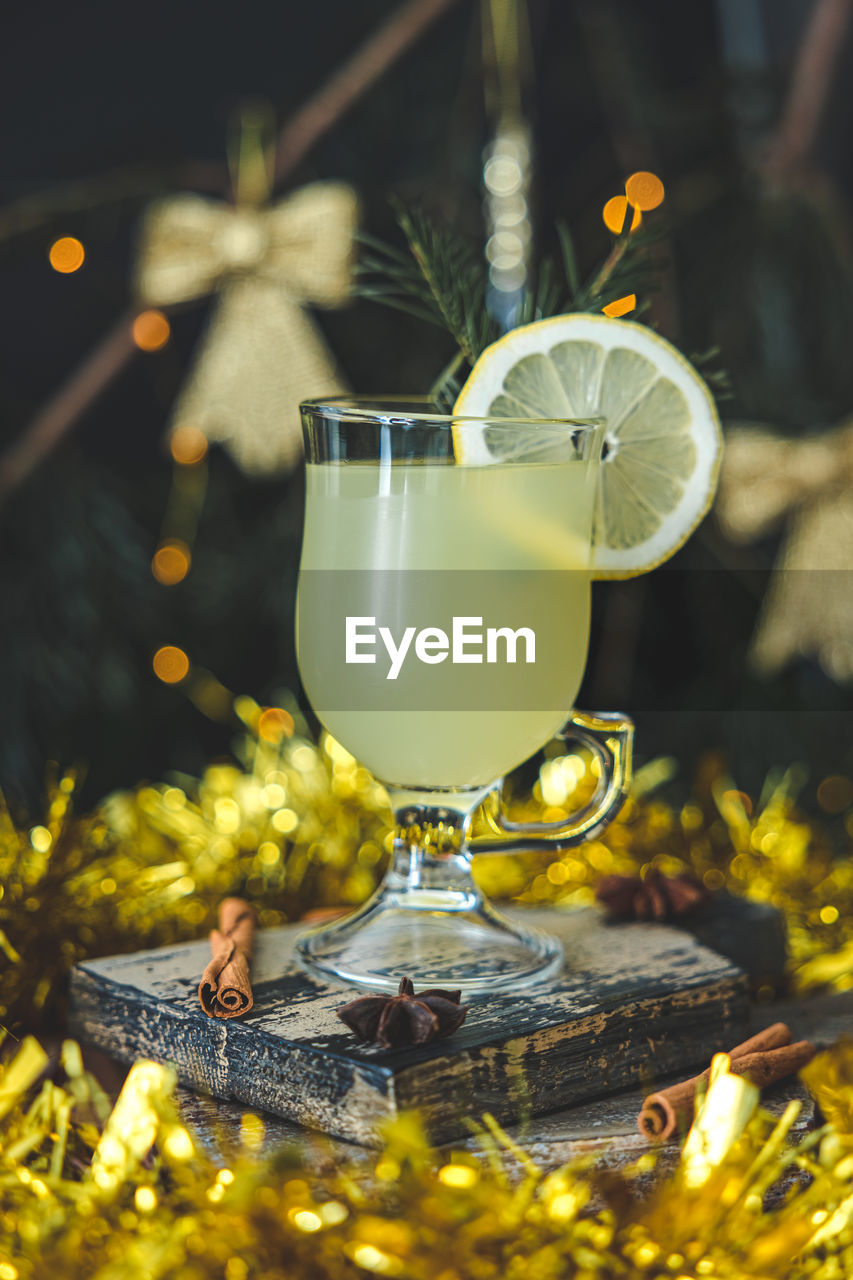 A glass of lemon drink with a circle of lemon and cinnamon sticks on a cutting board 