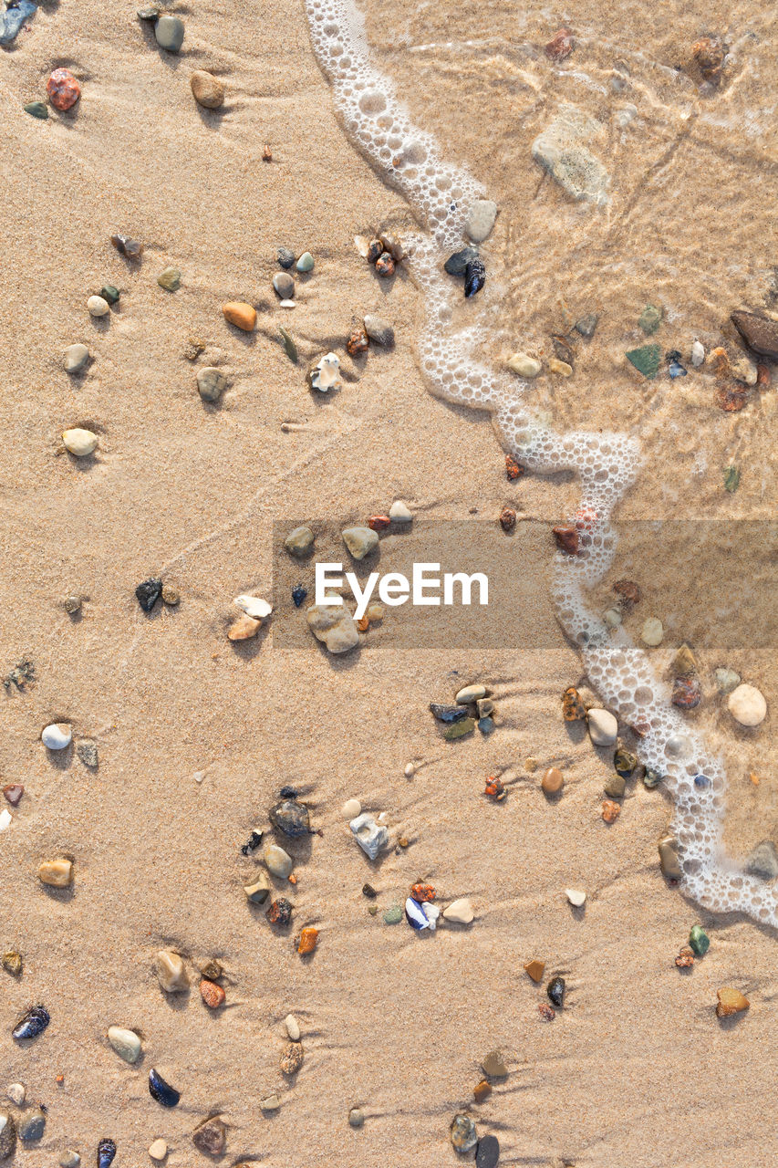 HIGH ANGLE VIEW OF PEBBLES ON SAND