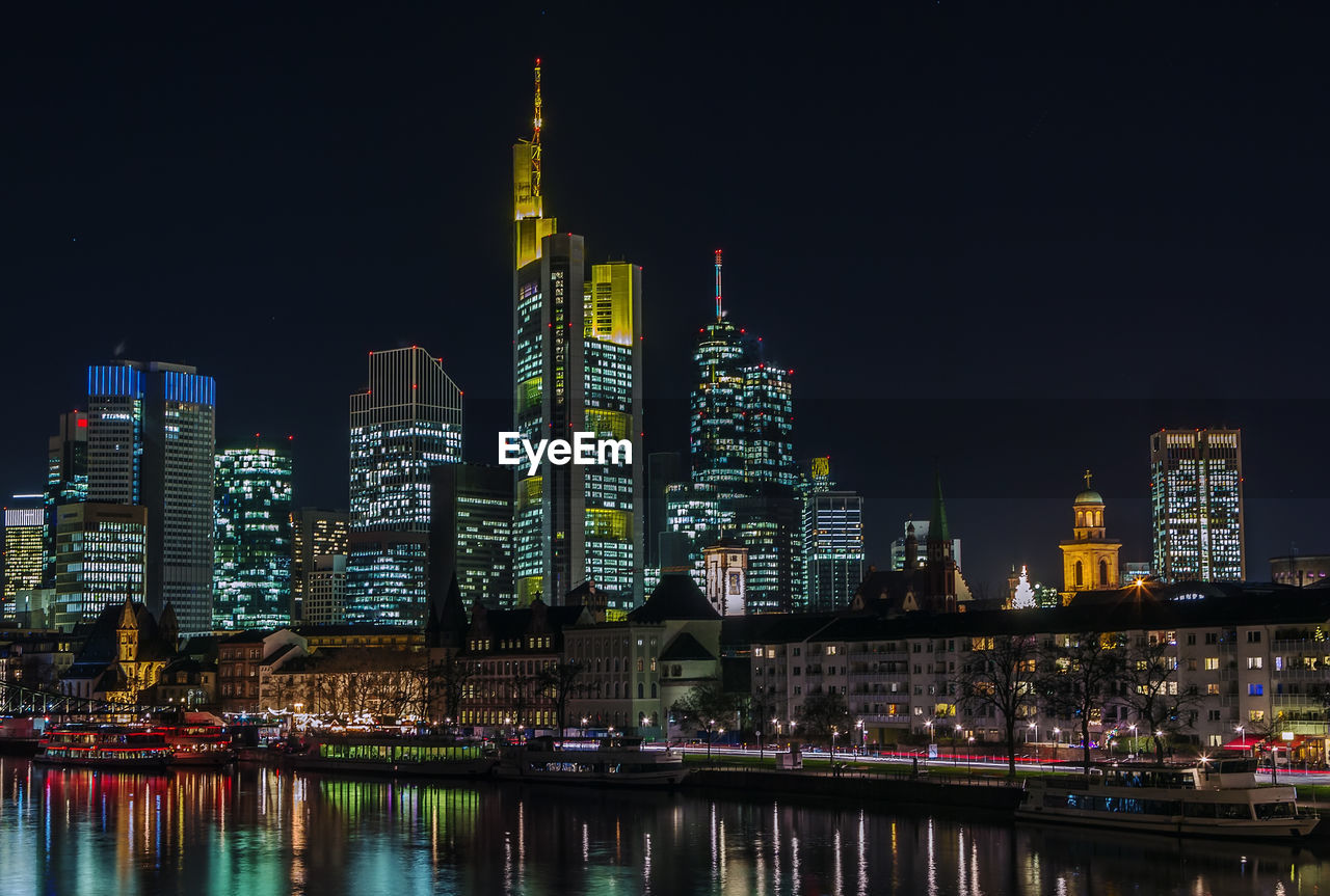 Illuminated buildings by river against sky in city at night