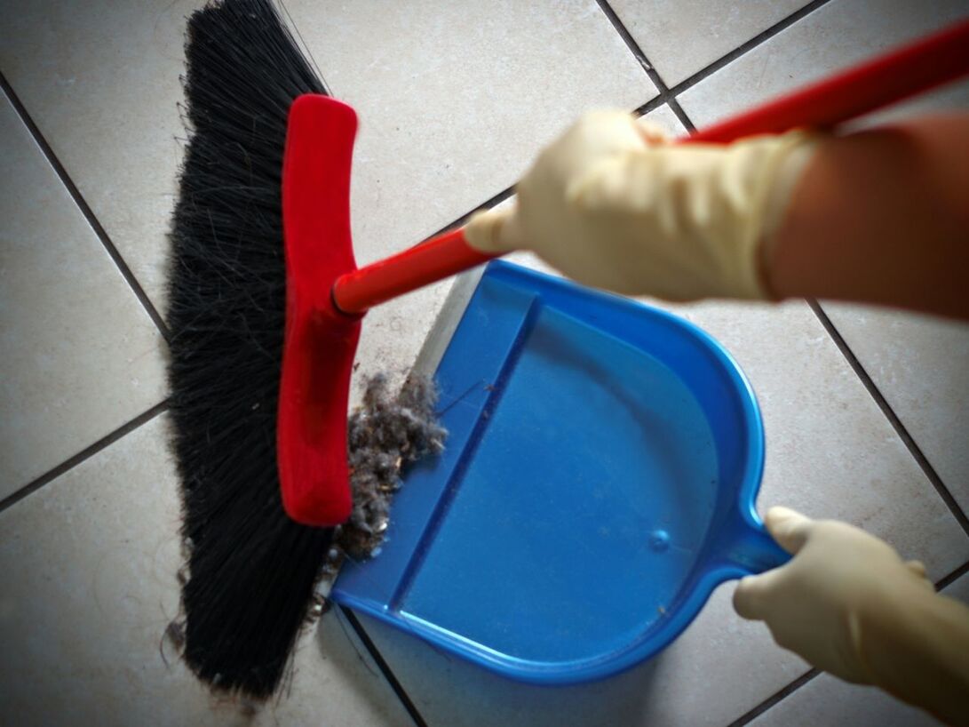 Close-up of gloved hands sweeping dust into dustpan tiled floor